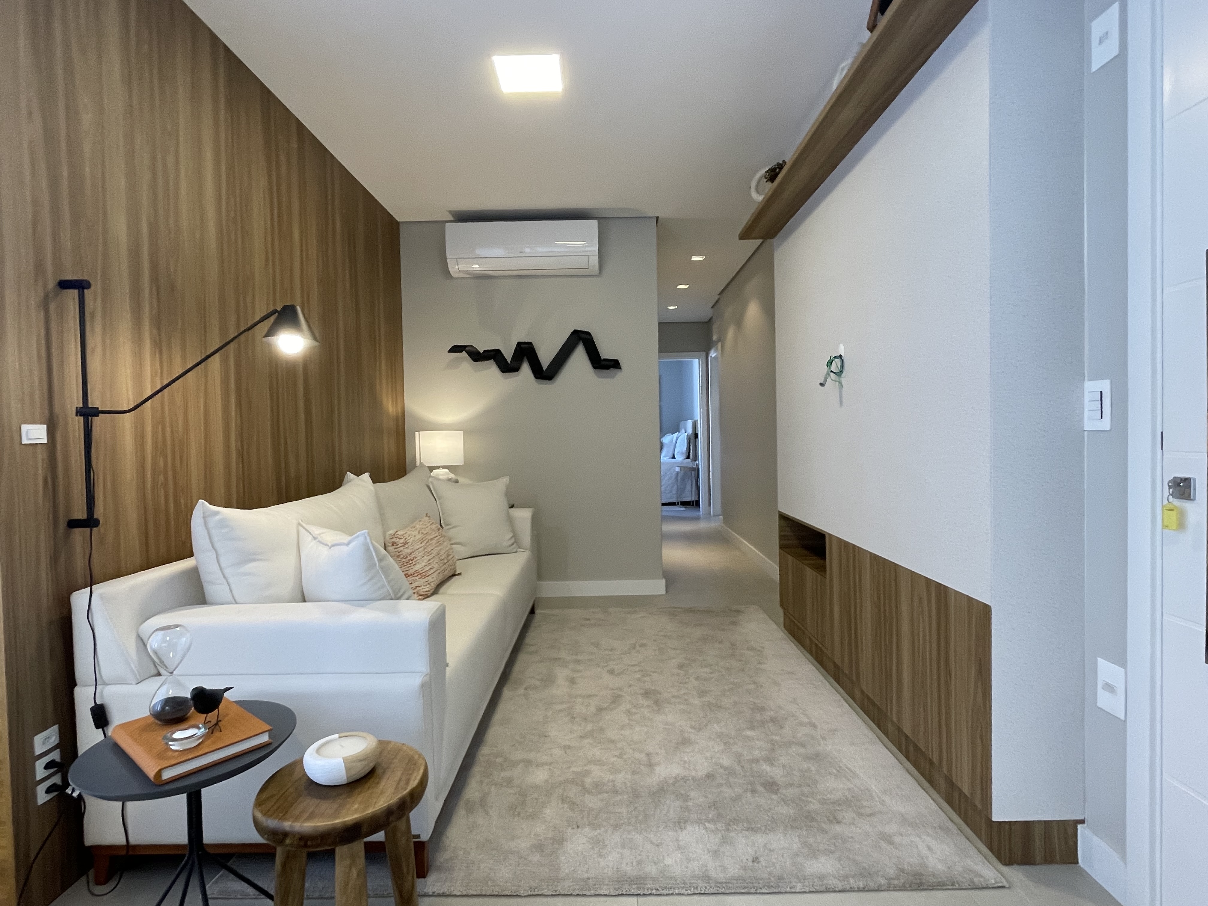 Apartamento decorado do Ed. Granada em tom refinado — sala de jantar com mesa de vidro, cadeiras de madeira e bancada com banquetas douradas.